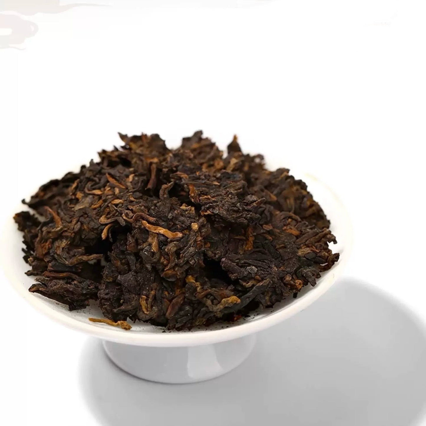 Dark brown tea leaves in a white bowl on a white background