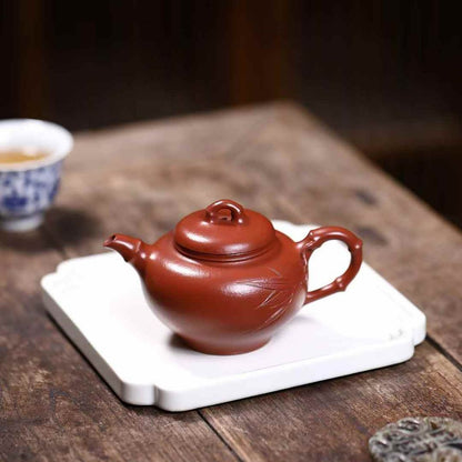 Yixing teapot on a porcelain tray placed on a wooden table. Blurred on the background a Chinese cup of tea